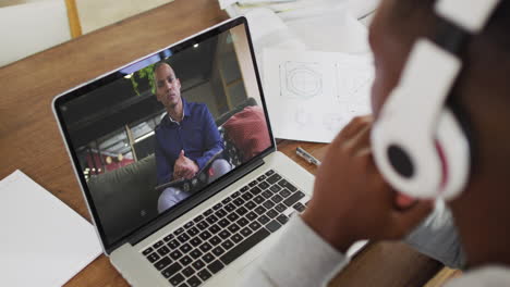african american businessman sitting at desk using laptop having video call with male colleague