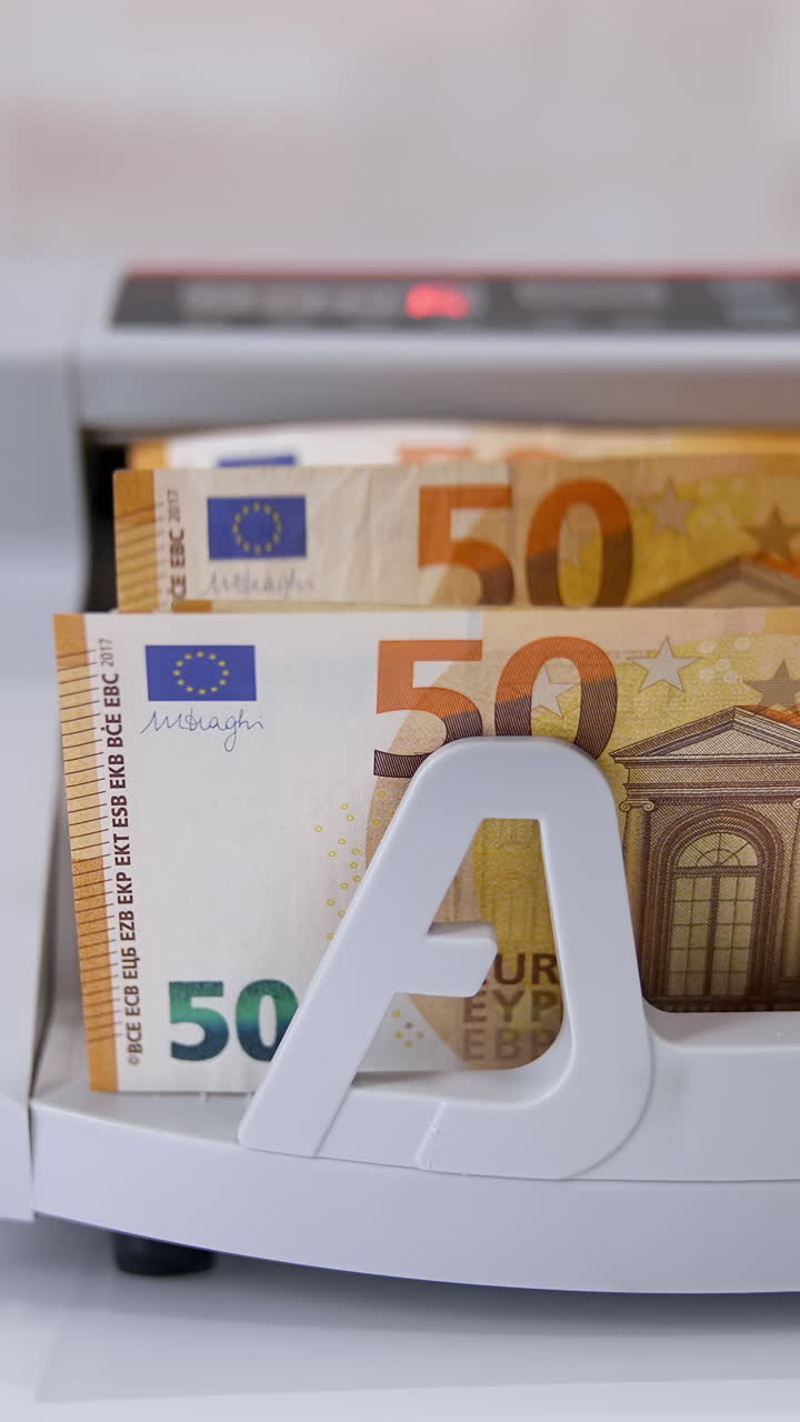 Electronic device is calculating fifty-euro bills. Woman puts paper banknotes into automatic counting machine. Automatic mechanism for bank financial operations. Currency exchange. Vertical video