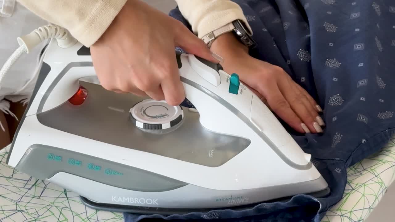 Close-up of female hands ironing a dark blue shirt with a modern steam iron