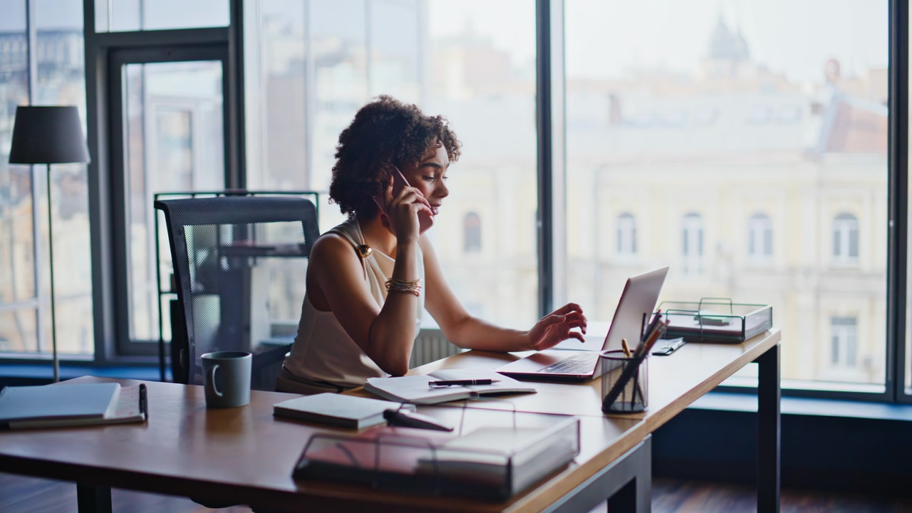 Businesswoman talking phone working laptop office. Woman multitasking busy desk.