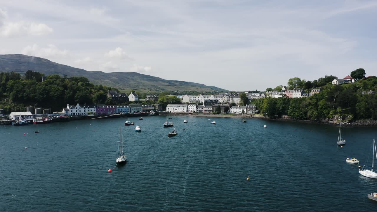 Drone shot pushing past boats approaching Scotland's shoreline with buildings spread across the coast