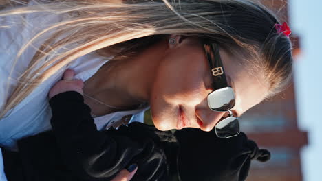 blonde woman wearing sunglasses and white shirt waves her baby. close up. vertical screen.