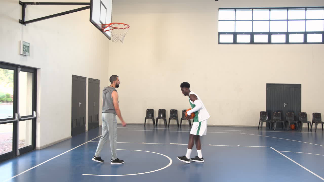 African american male basketball player catching and throwing basketball with coach in gym