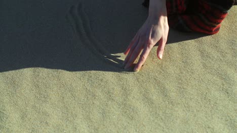 woman draws on the sand using her fingers