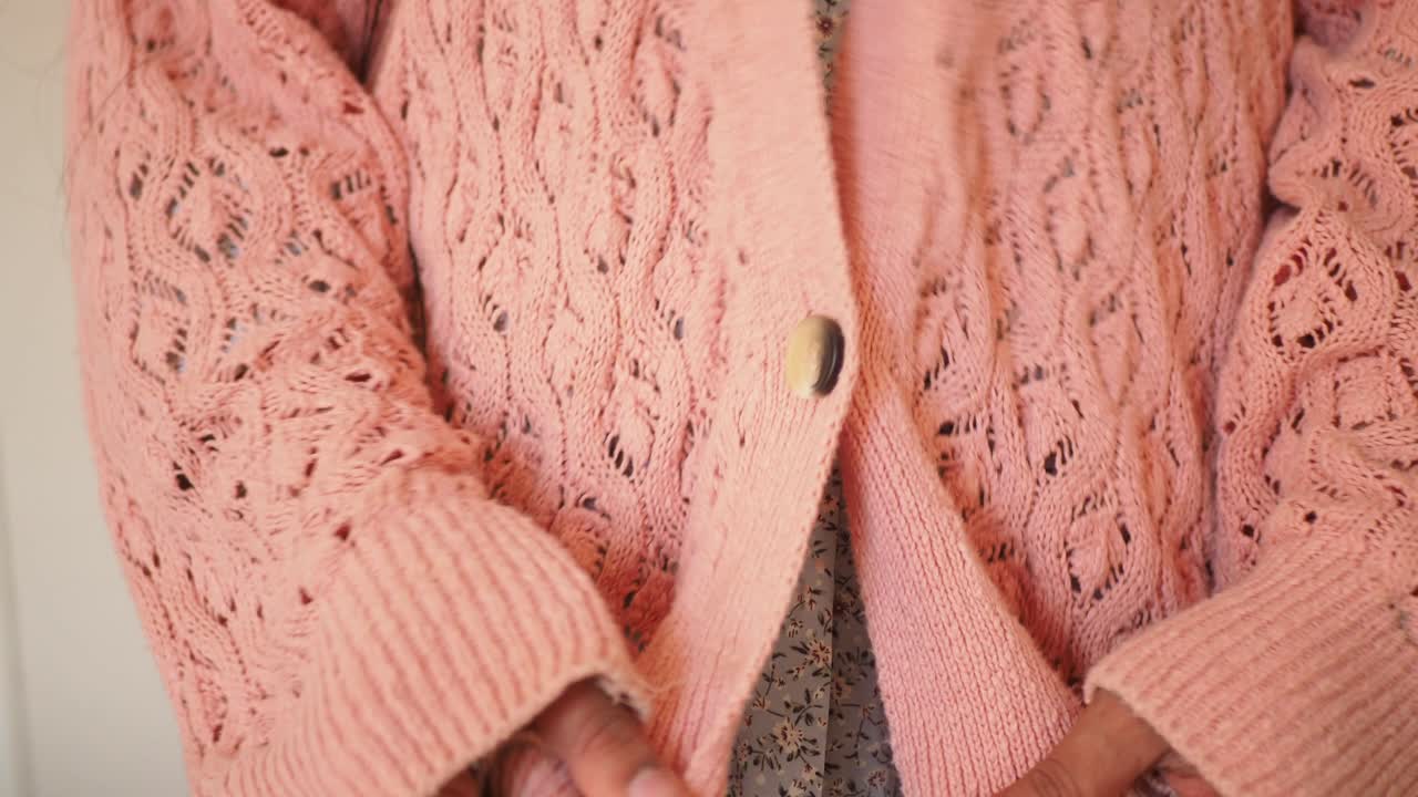 Close-up of a person wearing and adjusting a pink knitted cardigan