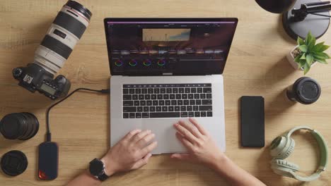 top view close up of male color grading's hands using a laptop next to the camera editing the video in the workspace at home