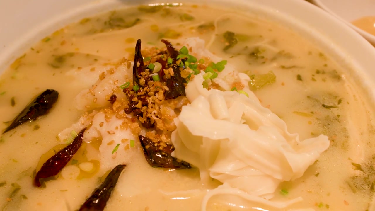 Spisepinde dypper hvid fisk i en krydret keramisk skål med bouillon og tørrede chilier