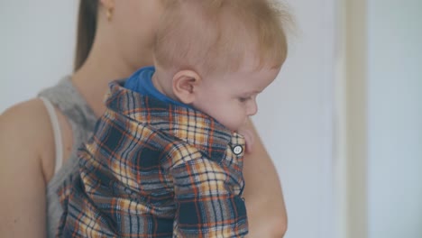 mommy-holds-lovely-baby-in-arms-against-wall-closeup