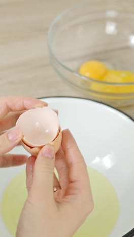 vertical close-up captures a hand delicately separating an egg yolk from the white using the shell, shown in slow motion for a smooth and clean division of ingredients for tiramisu dessert prep