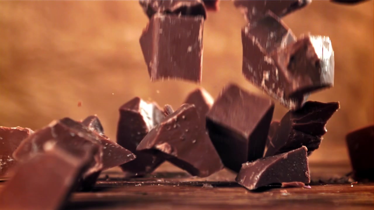 Movimento rallentato di pezzi di cioccolato fondente che cadono su una superficie di legno