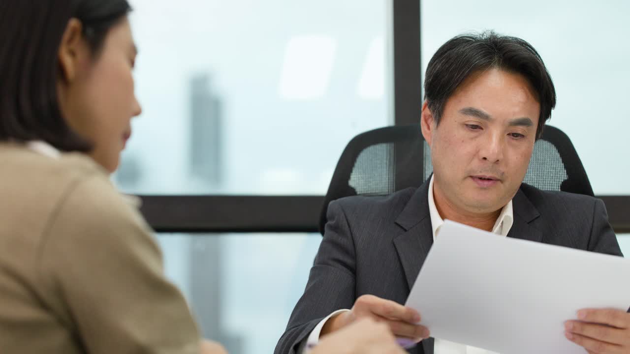 Two professionals discuss and analyze paperwork in a bright, modern office setting, natural lighting