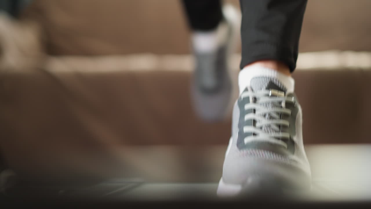 운동선수 여성은 트레드밀 세션에 참여합니다. 운동 신발을 입은 역동적인 여성은 체육 장비에서 조을 연습합니다. 활기찬 여성은 집에서 체력을 유지합니다.