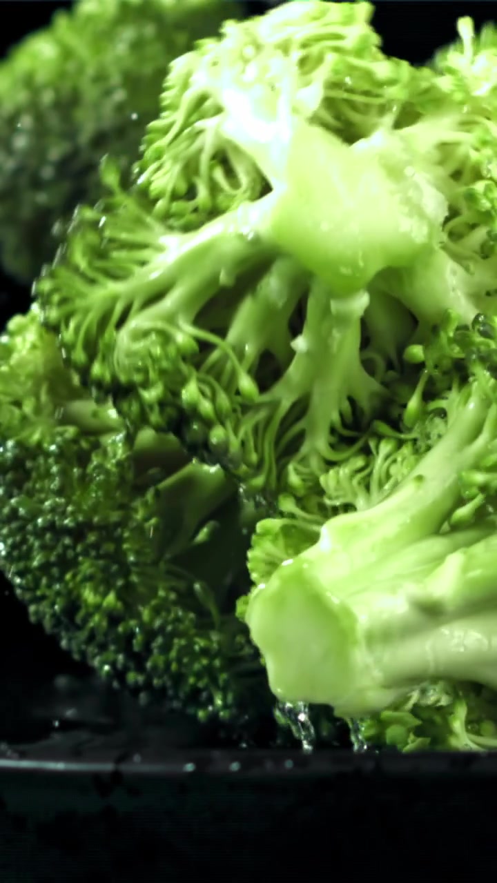 Cimette di broccoli freschi che cadono e schizzano acqua su sfondo nero