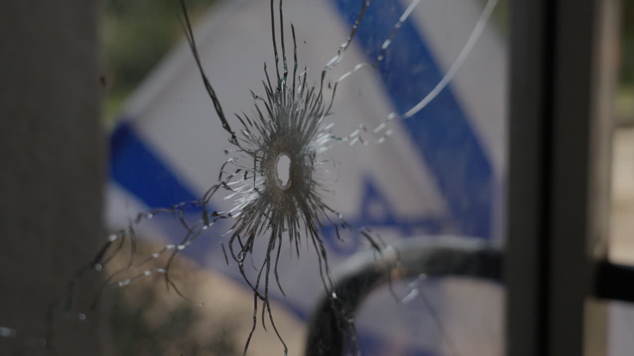 Broken glass window gunshot with Israeli flag in the background, Kibbutz Nir Oz after Hamas attack - slow motion