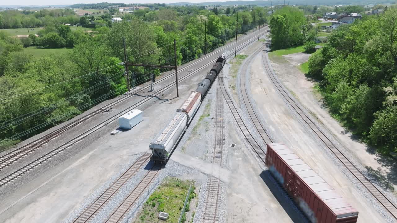 A vintage steam freight train makes its way backing up in yard performing switching operations moving steadily along the railway tracks in a peaceful countryside setting