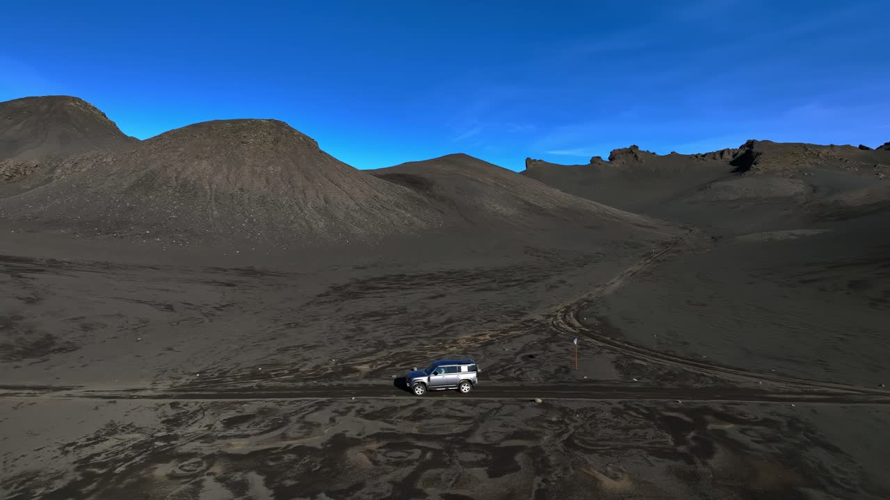 Ripresa con drone di un fuoristrada che inizia a guidare da fermo su una piana vulcanica nera e brulla in Islanda, circondato da montagne desolate. Concept di avventura remota “Lost in Iceland”