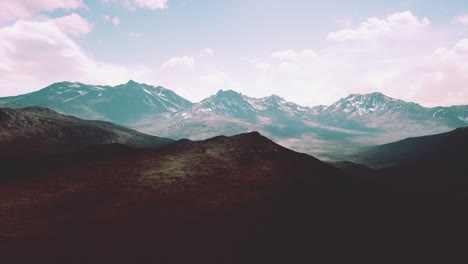 Aerial-Over-Valley-With-Snow-Capped-Mountains-In-Distance