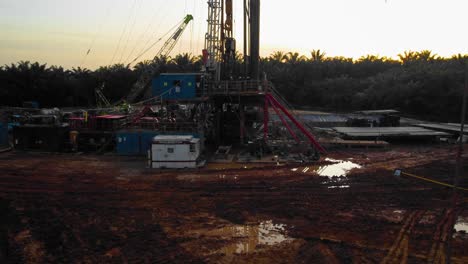 Cinematic-4K-Drone-Footage-of-Onshore-Drilling-Rig-equipment-structure-for-oil-exploration-and-exploitation-in-the-middle-of-jungle-surrounded-by-palm-oil-trees-during-sunset-and-high-oil-price