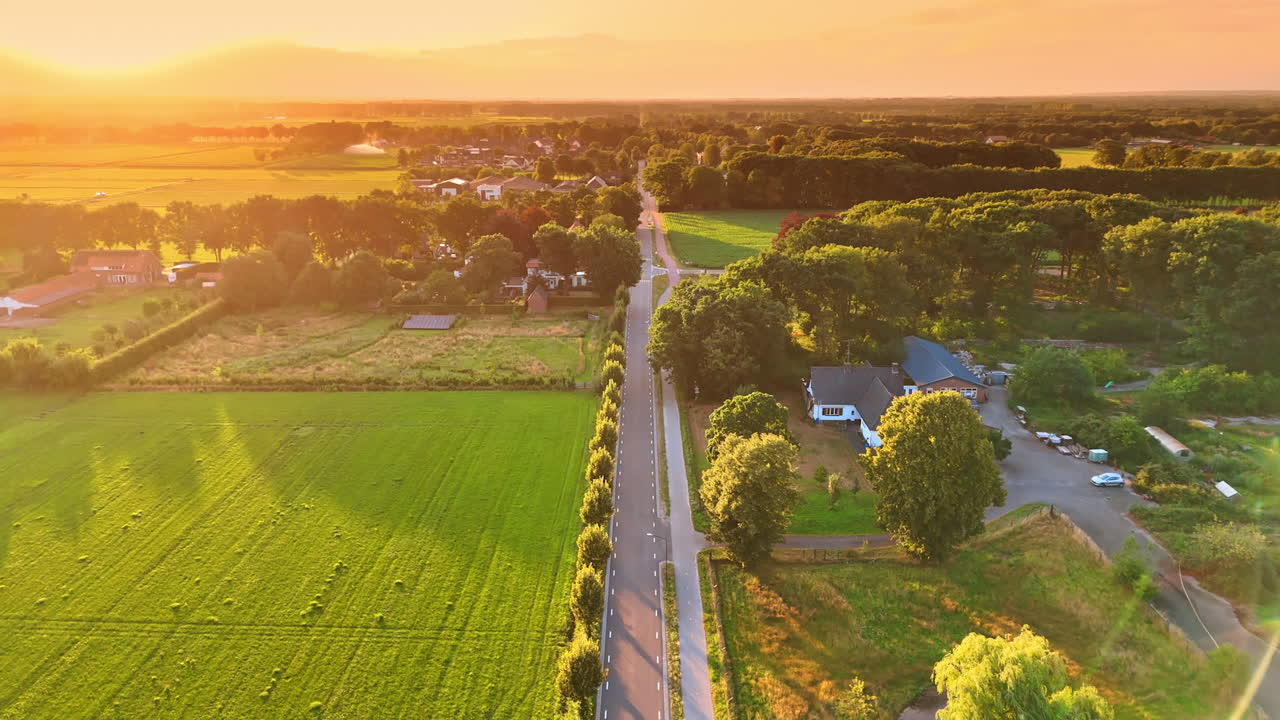 Dutch rural road leading through village and fields at sunset. Drone view of a rural Dutch road passing through fields and houses at sunset with warm golden light