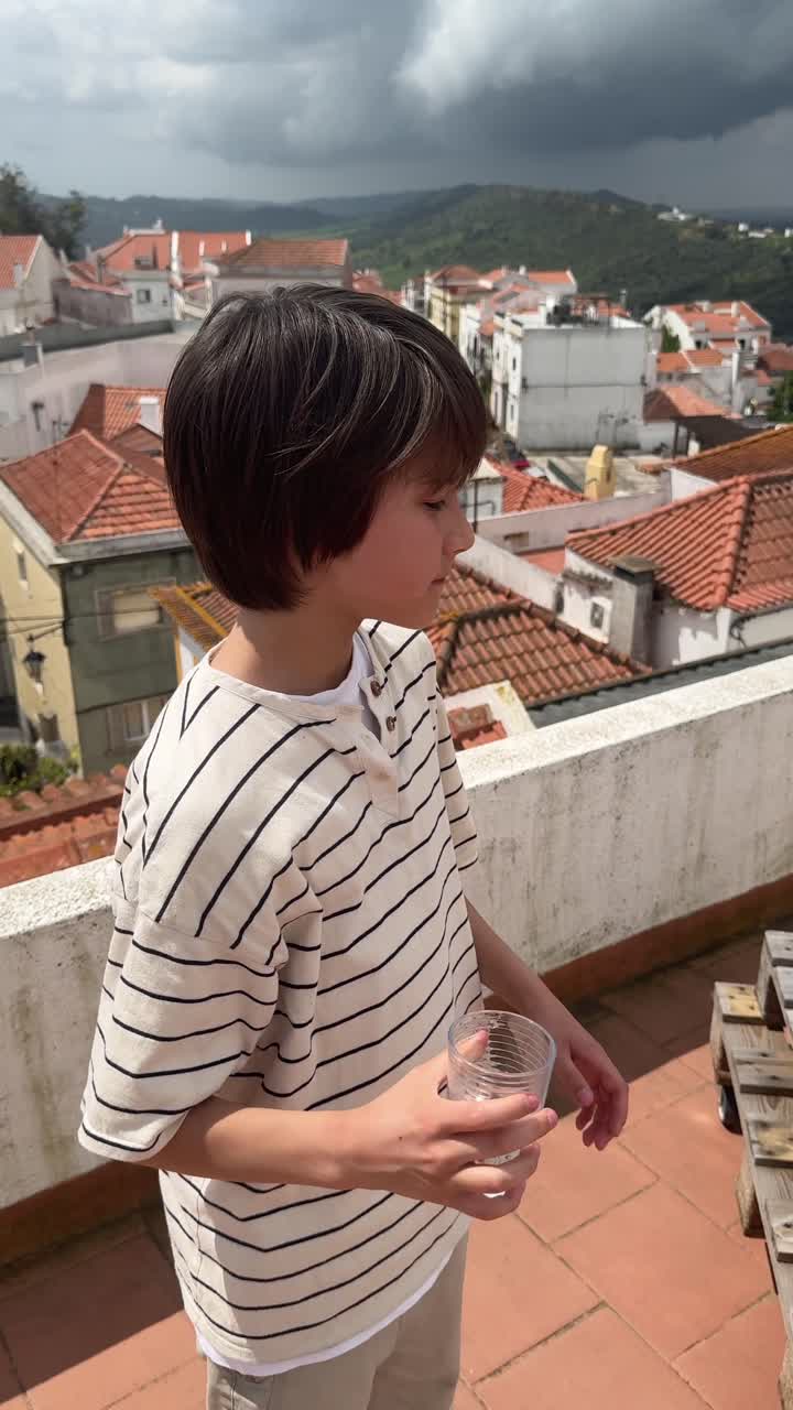 Boy Drinking Water on a Rooftop with City View