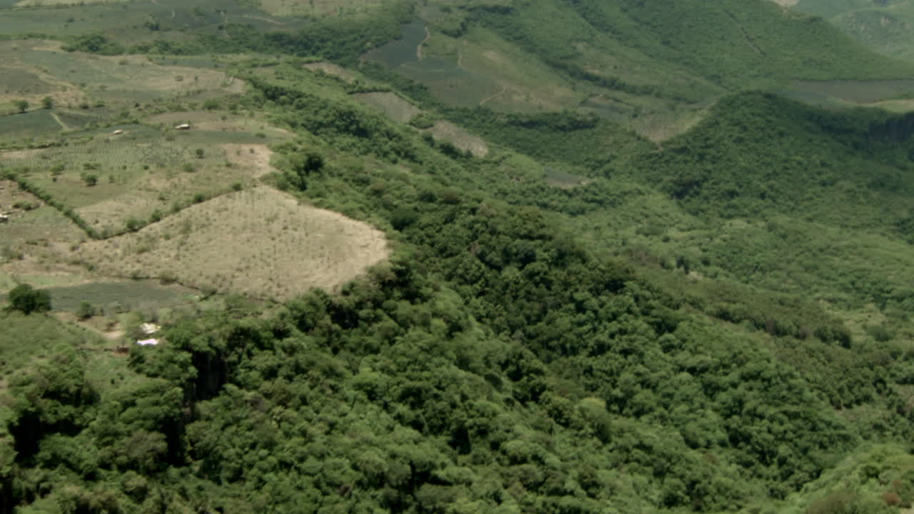 Aerial shot done with a hang glider with a motor flying over agave fields between the mountains of Tequila, Jalisco, Mexico.