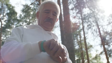 vista de ángulo bajo del hombre mayor con cabello gris y bigote caminando en el bosque y tocando la pantalla del reloj de pulsera de fitness