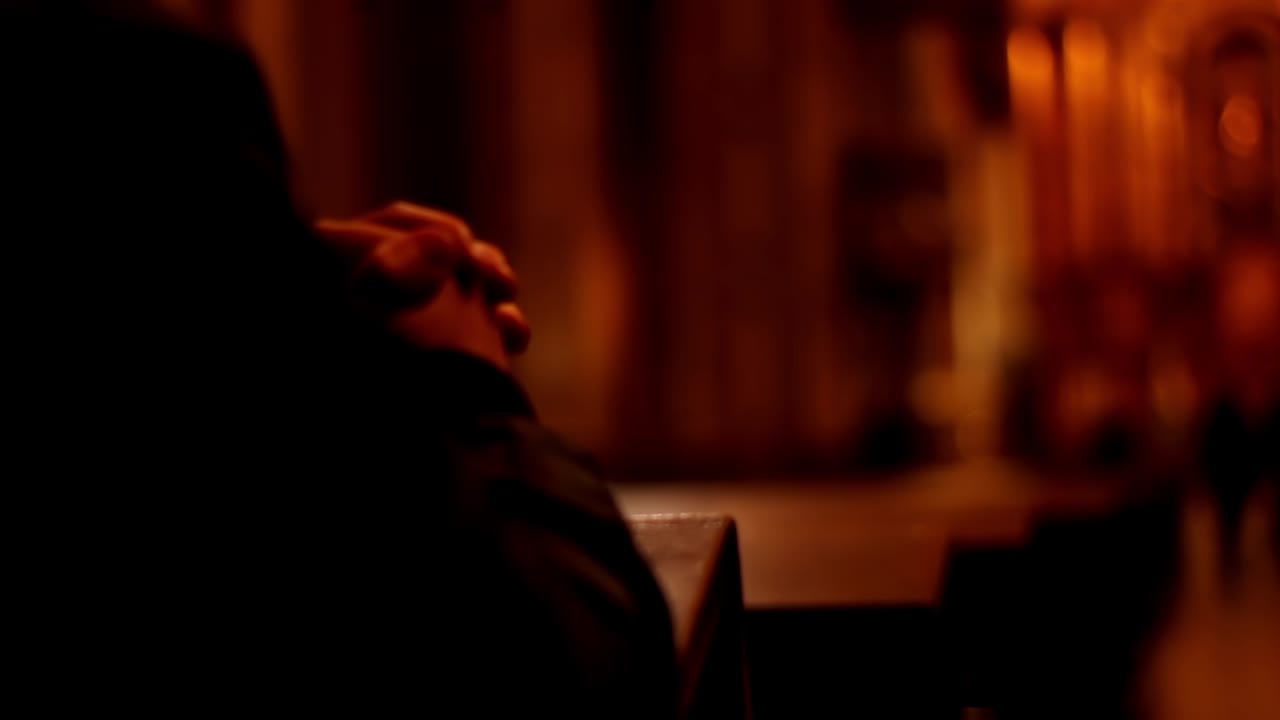 Persona che prega con le mani giunte in una chiesa in penombra.