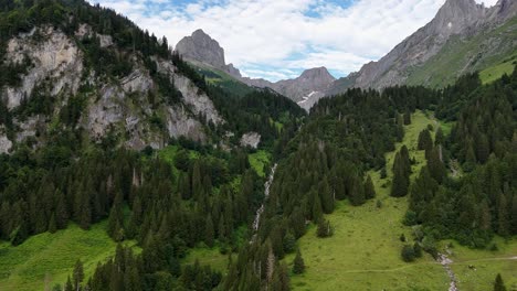 a lush green valley surrounded by rugged mountains and dense forests on a partly cloudy day