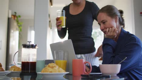 Pareja-De-Lesbianas-Caucásicas-Teniendo-Una-Videollamada-En-Una-Computadora-Portátil-Mientras-Desayunan-En-Casa