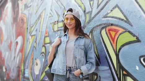 portrait shot of young caucasian stylish hipster girl standing at graffity wall and smiling at the camera