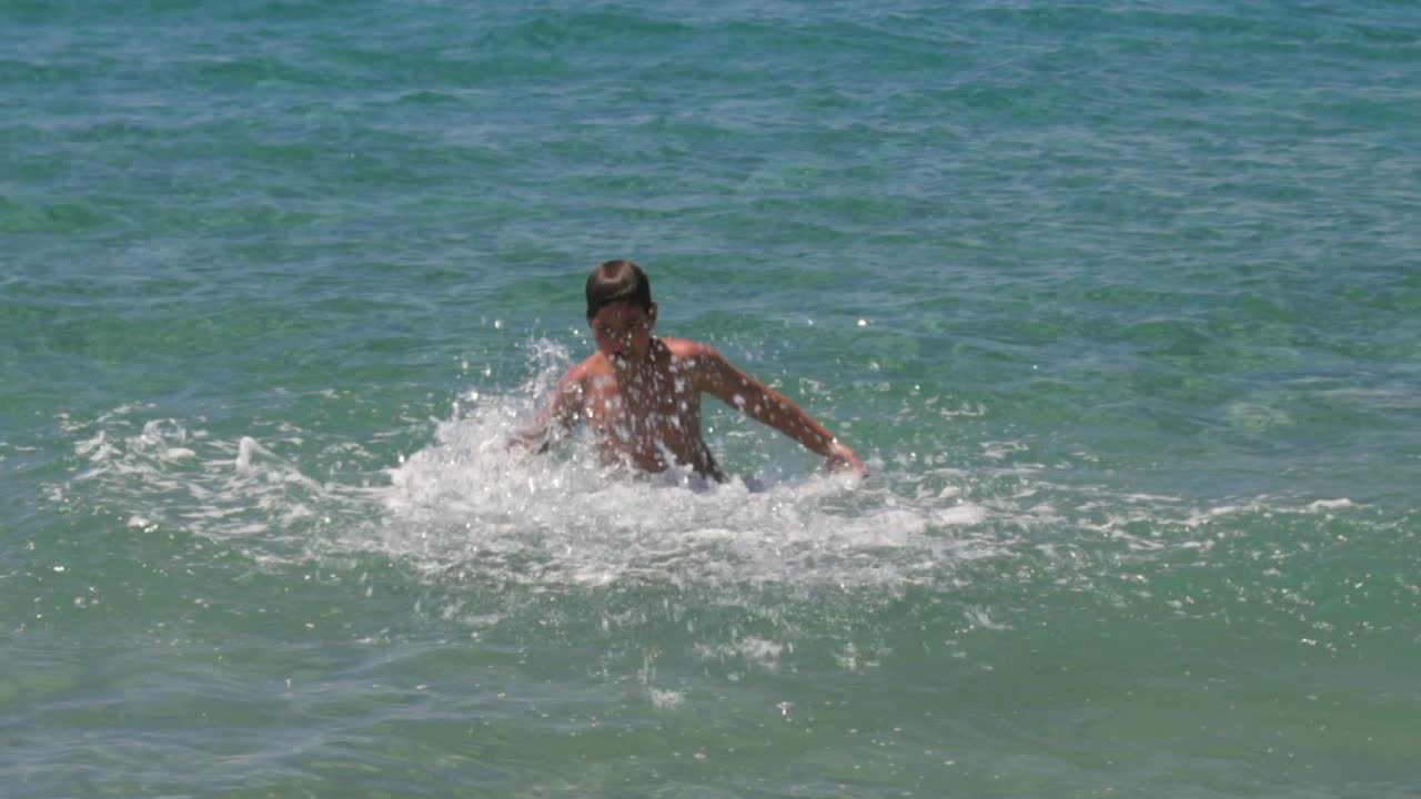 caucásico griego niño de 10 años, jugando en aguas marinas verdes claras, salpicando alrededor, 100 fps cámara lenta medio tiro