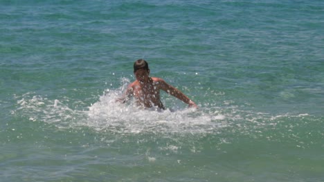 Caucasian-greek-10-years-old-boy,-playing-in-clear-greenish-sea-waters,-splashing-around,-100fps-slow-motion-medium-shot