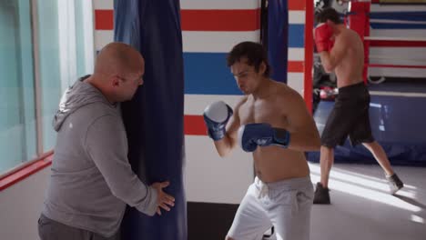 caucasian man using punchbag with coach in boxing gym