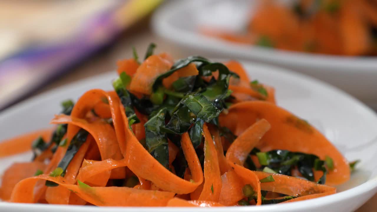 요리사가 토마토 페이스트, 당근 또는 병아리 콩을 넣은 주황색 파스타 국수에 신선한 파슬리 장식을 장식하거나 레스토랑이나 가정 주방에서 손을 닫고 파란색 고무 장갑을 끼고 요리합니다.