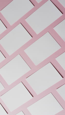 vertical video of white business cards arranged on pink background, copy space, slow motion