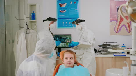 Madre-E-Hija-Con-Traje-Protector-Esperando-En-La-Sala-De-La-Clínica-Para-Un-Dentista-Pediátrico