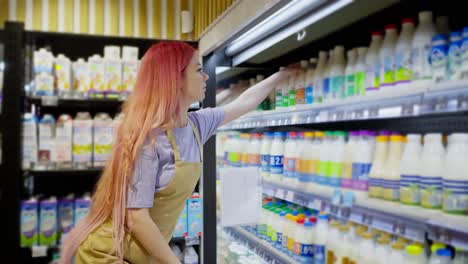 Side-view-of-a-girl-supermarket-worker-with-pink-hair-placing-goods-on-the-dairy-products-counter-in-a-supermarket