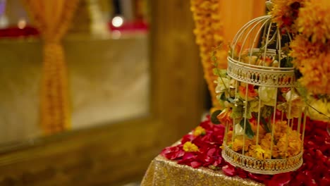 Marry-gold-flower-bouquet-set-in-a-cage-with-Candles-in-glasses-and-rose-petals-on-the-table,-Panning-view