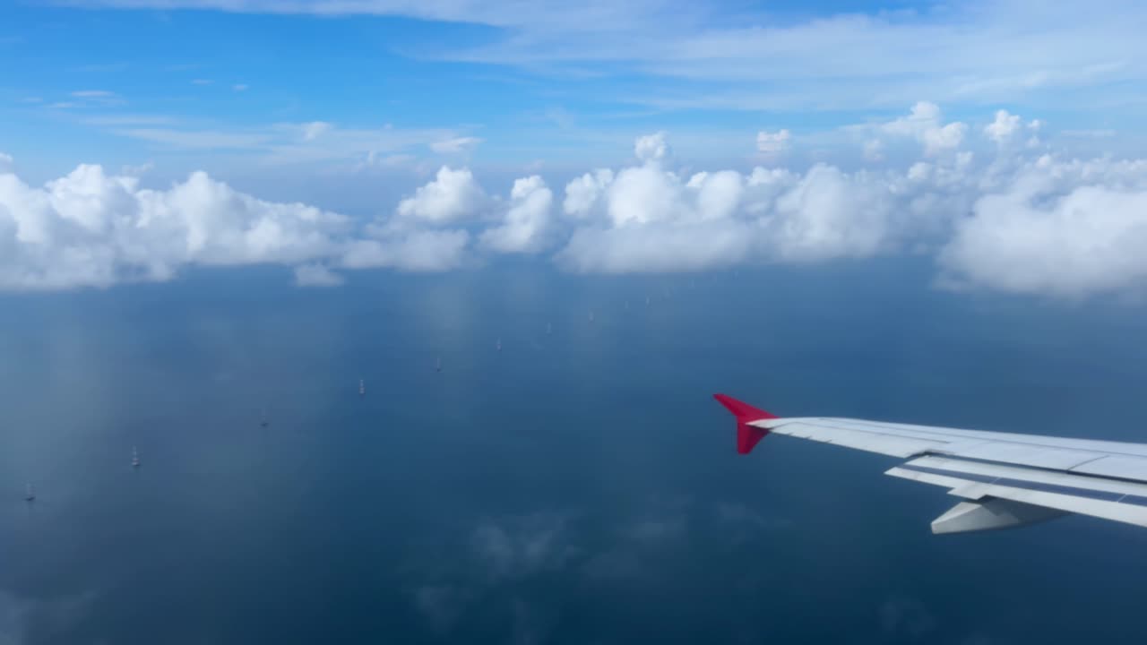 Airplane wing over clouds and ocean, serene sky view