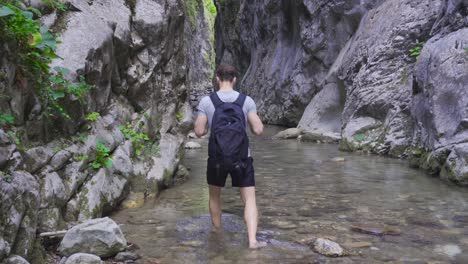 Young-man-walking-in-running-water-in-canyon,-barefoot.