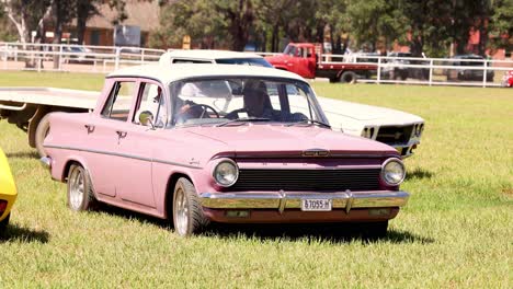 classic pink car driving across a grassy area