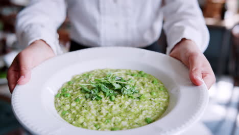 Nahaufnahme-Einer-Restaurantkellnerin,-Die-Einen-Teller-Erbsenrisotto-Hält