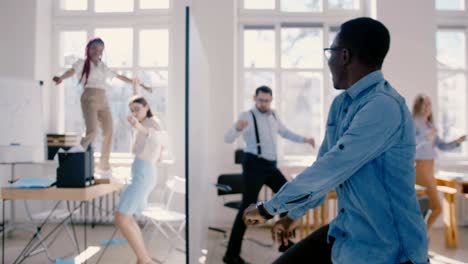 feliz empresario afroamericano emocionado haciendo divertido baile de celebración loco, compartir el éxito con sus colegas en cámara lenta.
