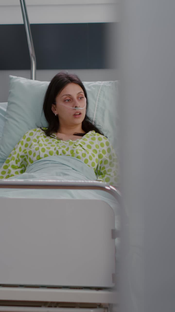 Vertical video: Caucasian female with nasal oxygen tube sitting in bed in hospital ward