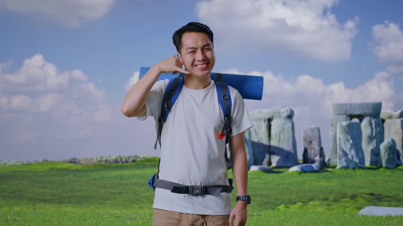 Asian Male Hiker With Mountaineering Backpack Smiling And Showing Call Me Gesture While Traveling In Stonehenge