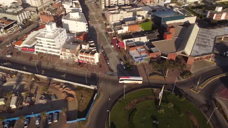 Toma-Aérea-De-Arriba-Hacia-Abajo-Del-Autobús-Turístico-Conduciendo-En-La-Rotonda-De-La-Ciudad-De-Punta-Del-Este-A-La-Luz-Del-Sol,-Uruguay