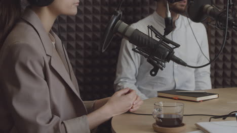 detalle de las manos de una joven elegante jugando con su anillo de bodas mientras un hombre habla en un micrófono de estudio de radio