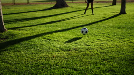 a female soccer player kicking a football to her teammate on a grass sport field in slow motion