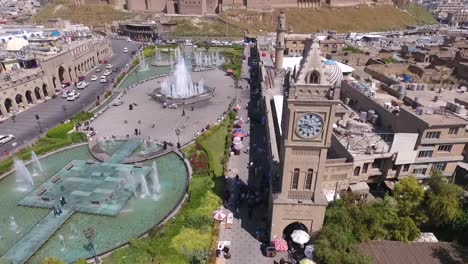 an aerial shot of the city of erbil showing the ancient erbil citadel and the garden opposite the castle with water fountains and the popular market