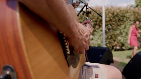 A-musician-strums-his-acoustic-guitar-amidst-fellow-bandmates,-enchanting-the-audience-at-a-music-festival-nestled-in-the-tranquil-countryside-of-a-stunning-winery